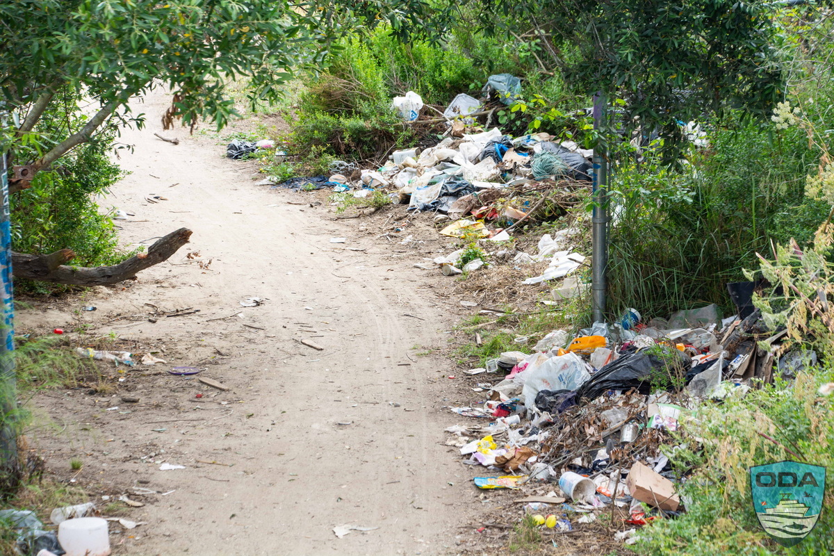 Trail to riverbed lined with piles of trash